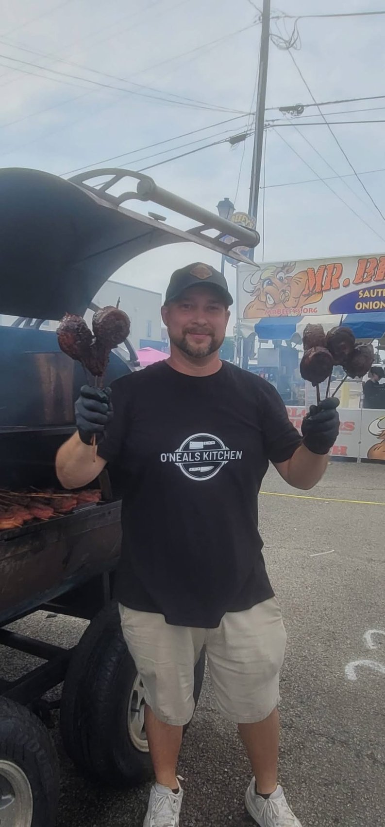 Original photograph of Brandon at a BBQ event holding smoked pork belly lollipops